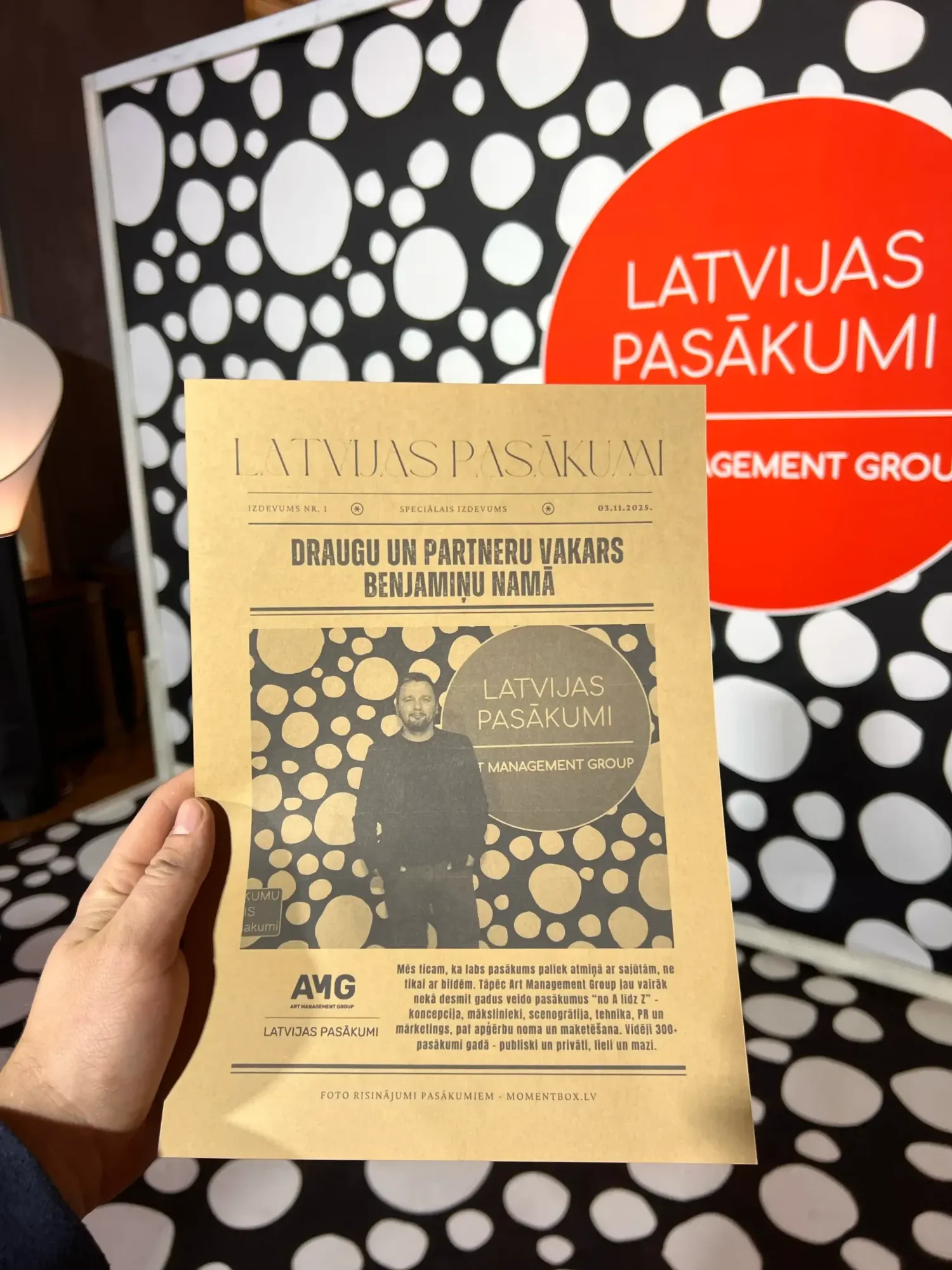 Latvijas Pasākumi: draugu un partneru vakars. Art Management Group vakars Benjamiņu namā. Avīzes galvā pasākuma zīmols, pirmajā lapā viesis pie foto sienas. 2025. gada novembris.
